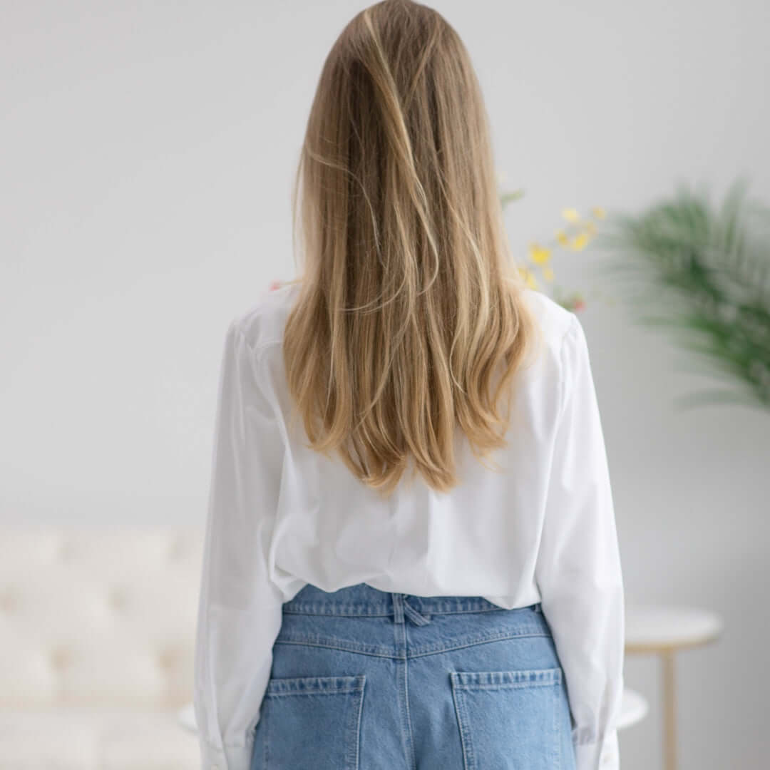 Woman wearing a classic white adaptive blouse from the back, featuring long hair and casual denim jeans.