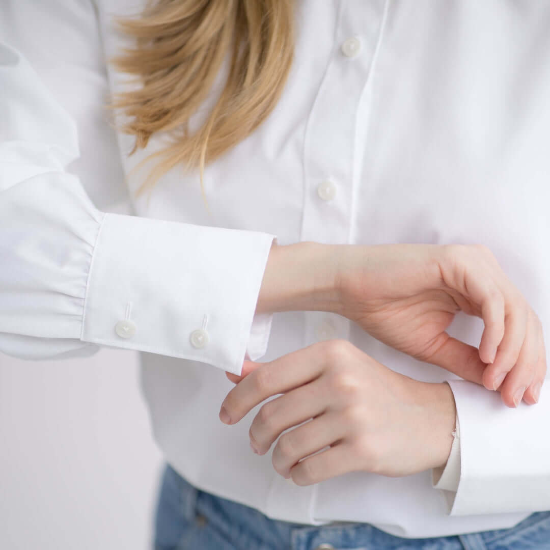Close-up of a woman adjusting the cuff of a classic white adaptive blouse with button details.