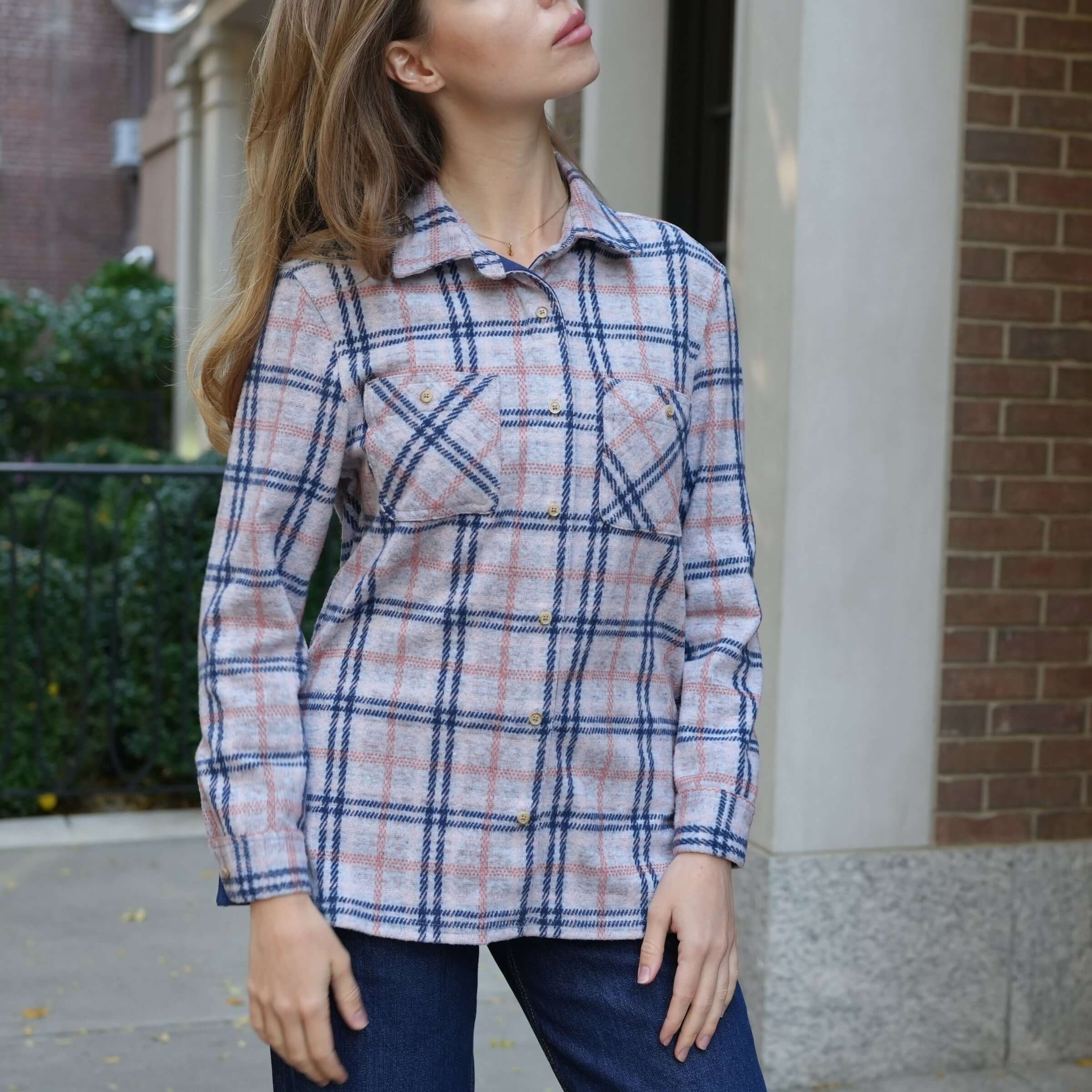 Women's pink, navy, and gray flannel shirt with a curved hem and buttoned pockets, styled outdoors.