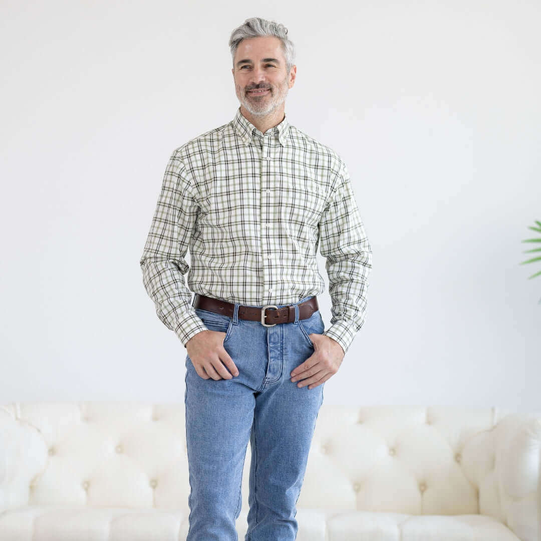 Man in green and black plaid long sleeve shirt with button-down collar, wearing blue jeans and smiling.