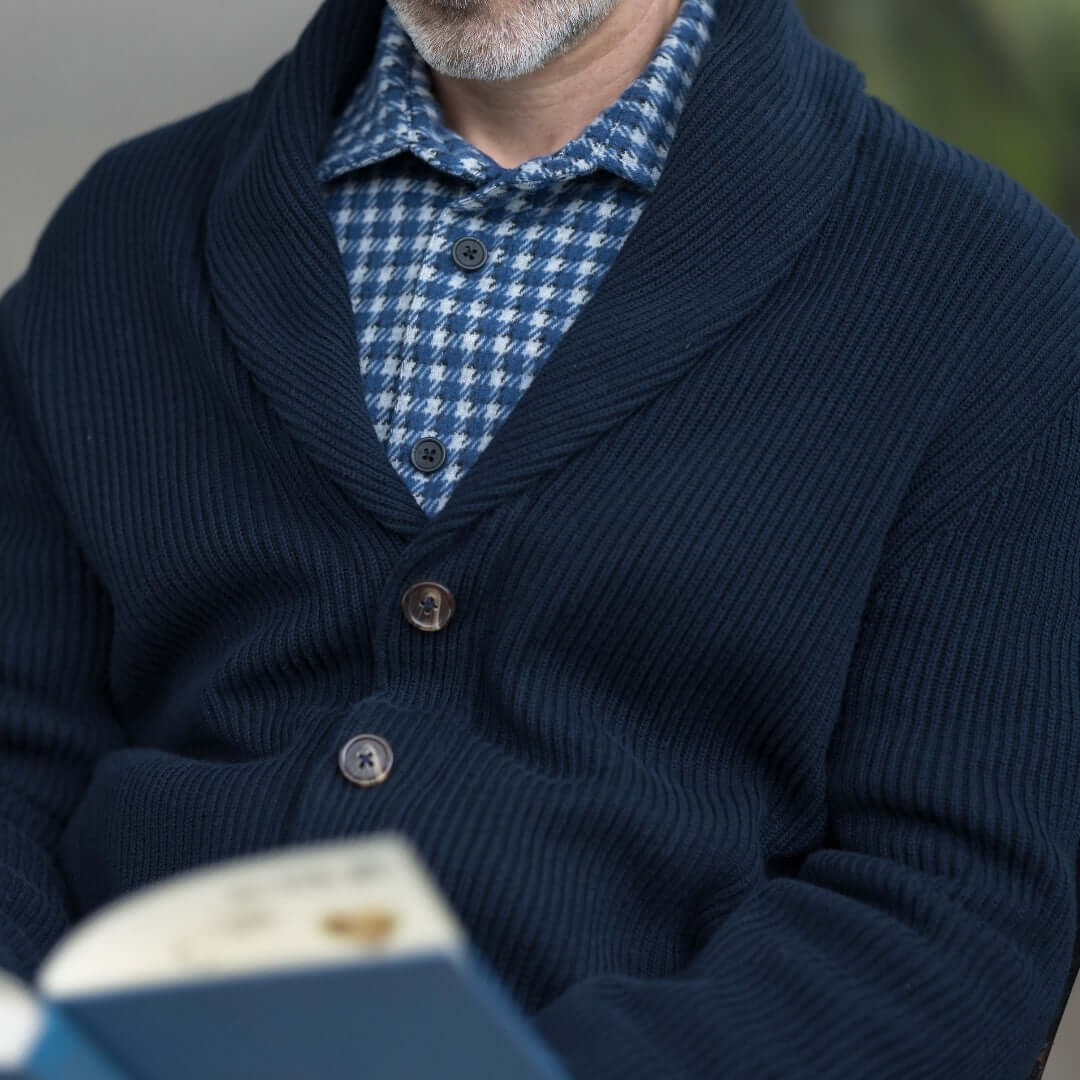 Man enjoying a book in a navy ribbed shawl collar cardigan with magnetic buttons and a checkered shirt.