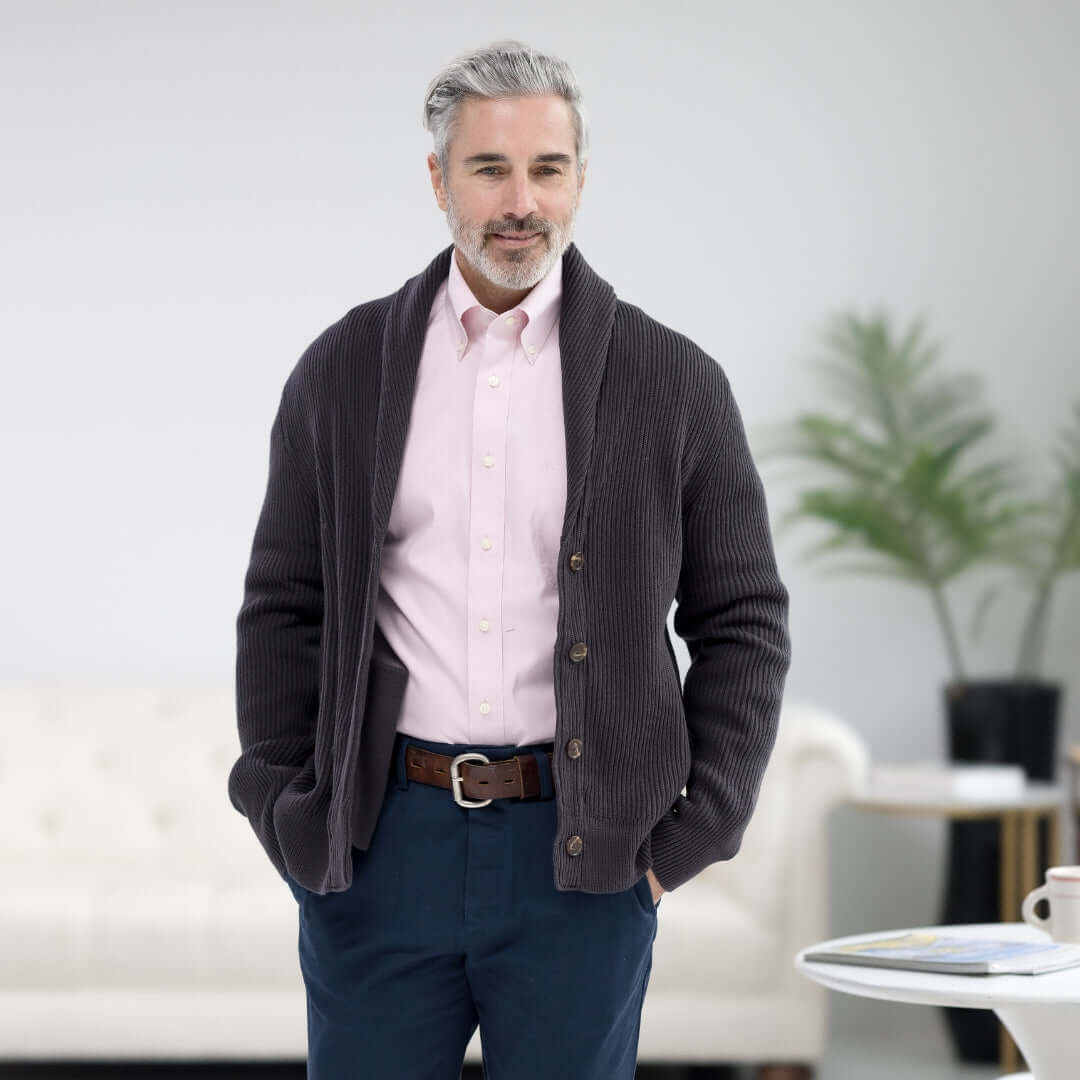 Man in grey ribbed cardigan with shawl collar and magnetic buttons, paired with a pink shirt and blue pants.