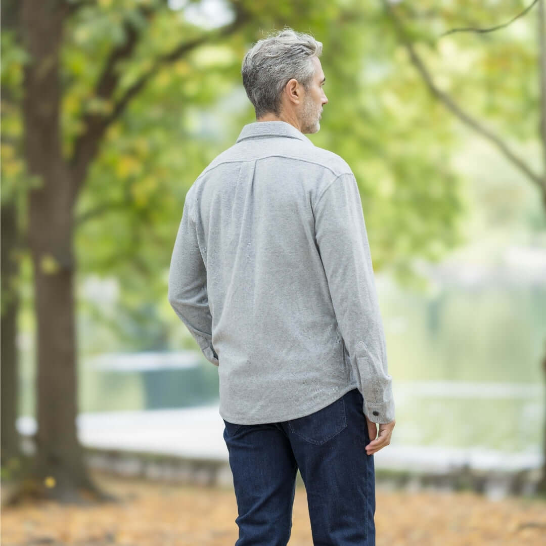 Man wearing a grey flannel shirt, standing outdoors with trees in the background, showcasing a casual style.