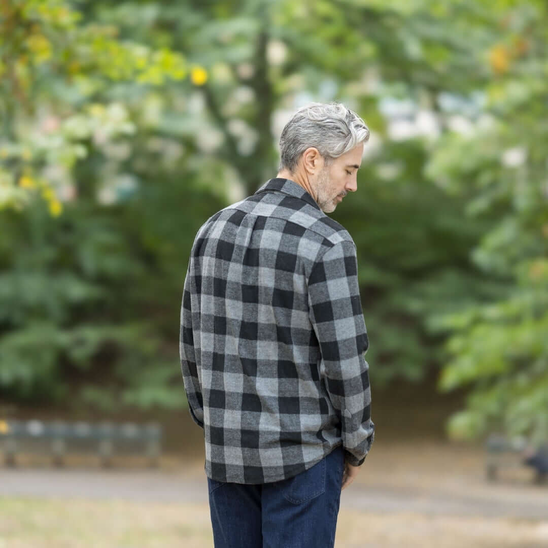 Man wearing a black buffalo check flannel shirt in an outdoor park setting, showcasing a stylish layering piece.