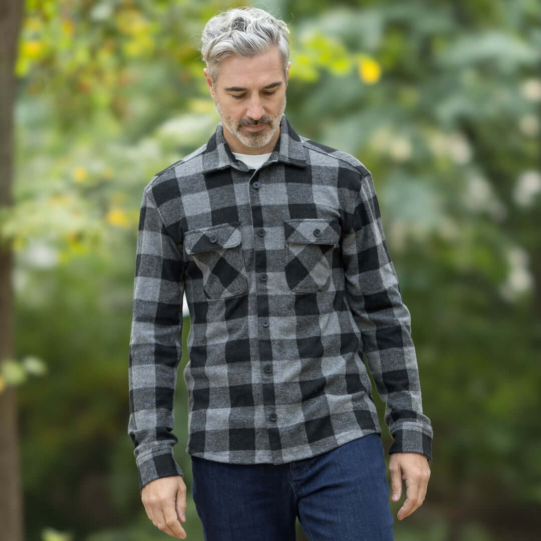 Man in a black buffalo check flannel shirt walking outdoors in a natural setting.