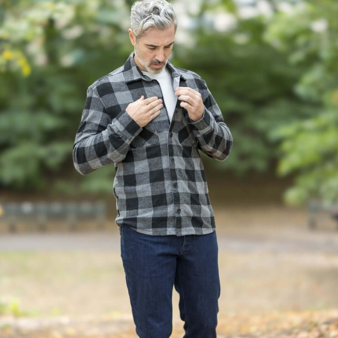 Man wearing adaptive black buffalo check flannel shirt, showcasing magnetic closures in a park setting.