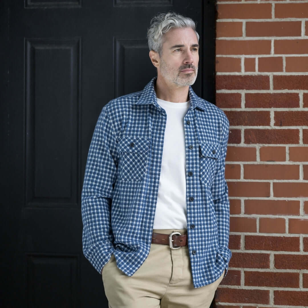 Man in a white and navy check flannel shirt standing against a brick wall, showing stylish layering options.