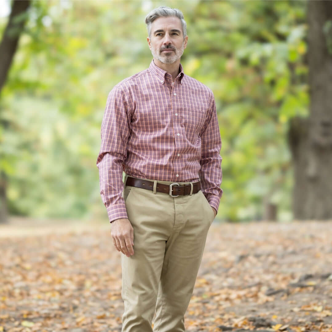 Man in a plaid button-down shirt and khakis standing outdoors in a park during autumn.