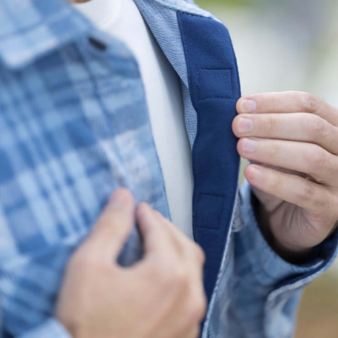 Close-up of a man's hands adjusting magnetic closures on a pale blue plaid flannel shirt.