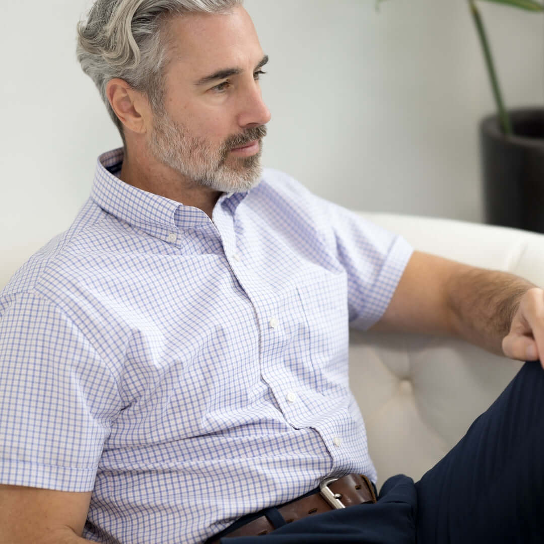 Man wearing a short sleeve plaid shirt, sitting comfortably on a sofa, showcasing a relaxed style.