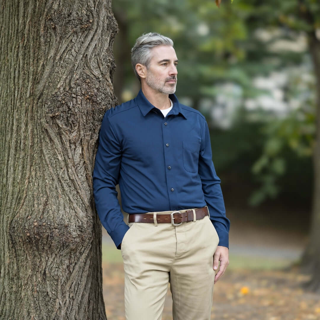 Man in adaptive true navy long sleeve cooling tech polo leaning against a tree in a natural outdoor setting.