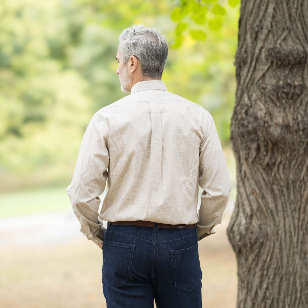 Back view of a man wearing a beige check long sleeve button down collar shirt in an outdoor setting.