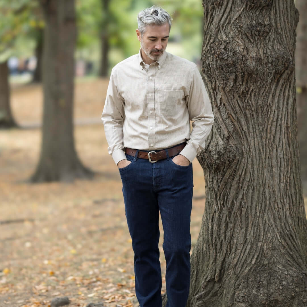 Man wearing a beige check long sleeve shirt with a button-down collar, standing by a tree in a park.