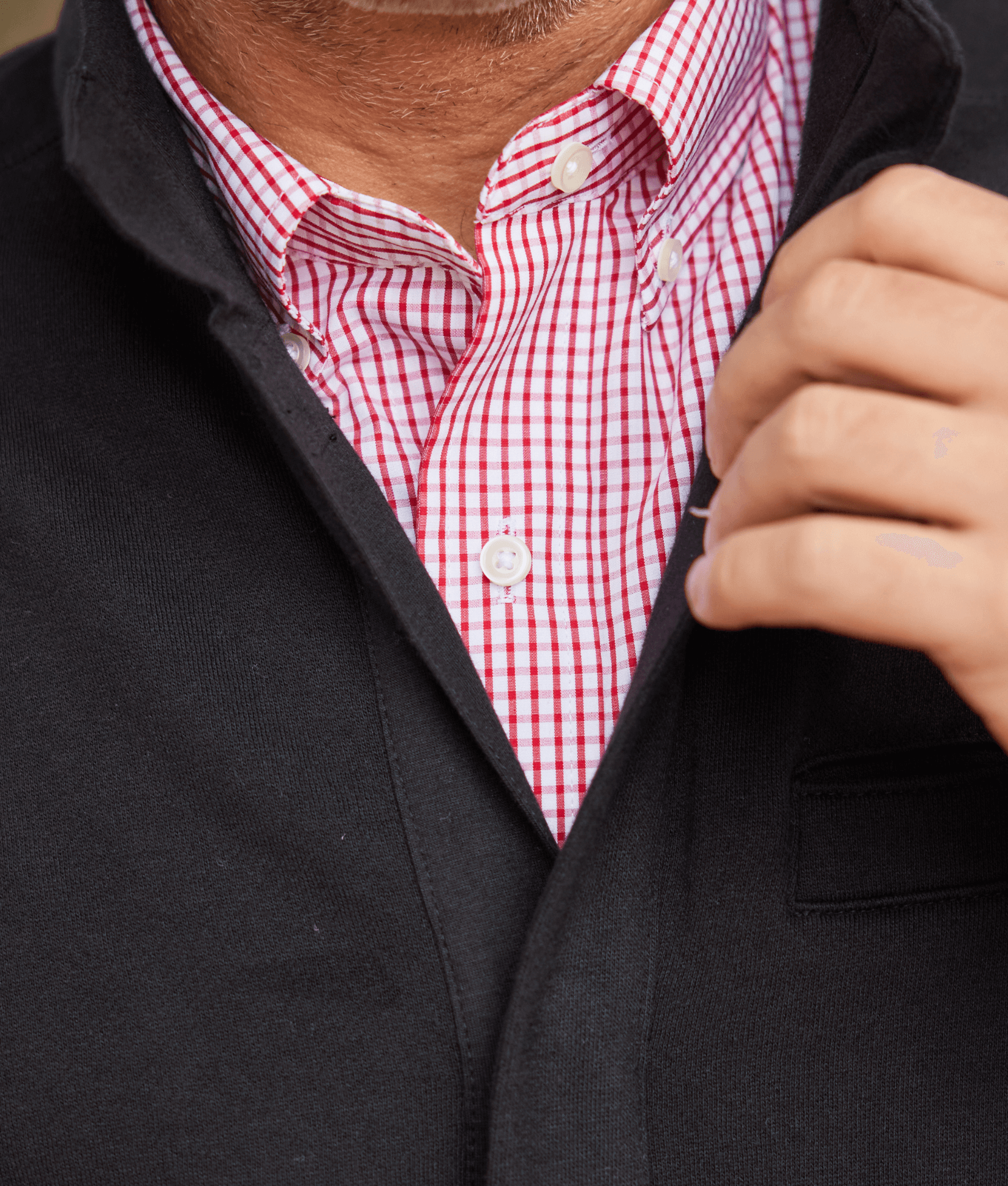 Close-up of a man wearing a black knit fleece Dillon jacket over a red and white checked shirt.