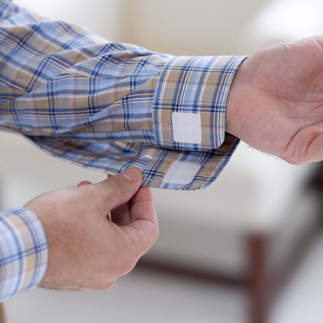 Close-up of a hand adjusting the Velcro closure on a blue and brown plaid shirt sleeve.