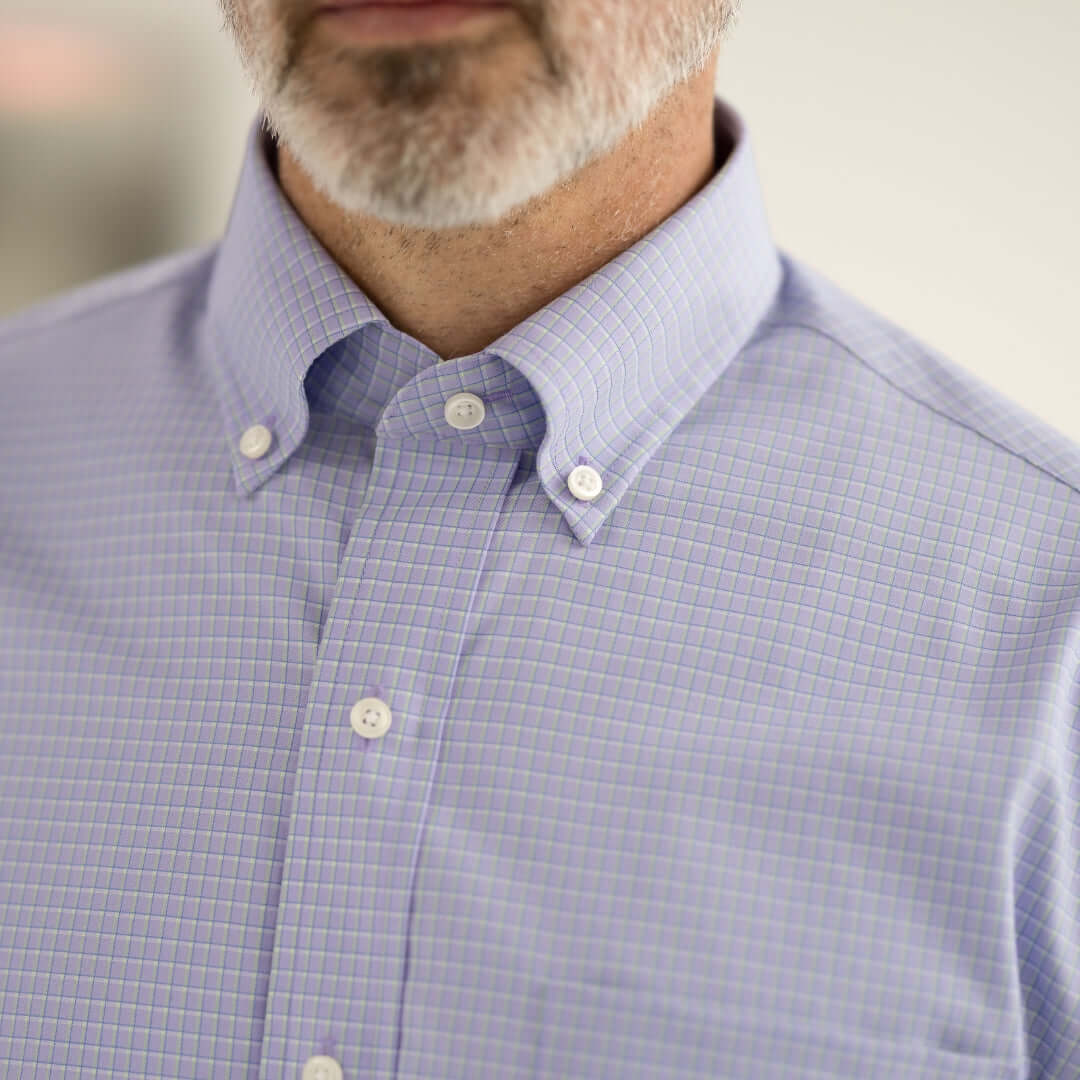 Close-up of a man wearing a light purple checked button-up shirt, showcasing its stylish collar and fabric texture.