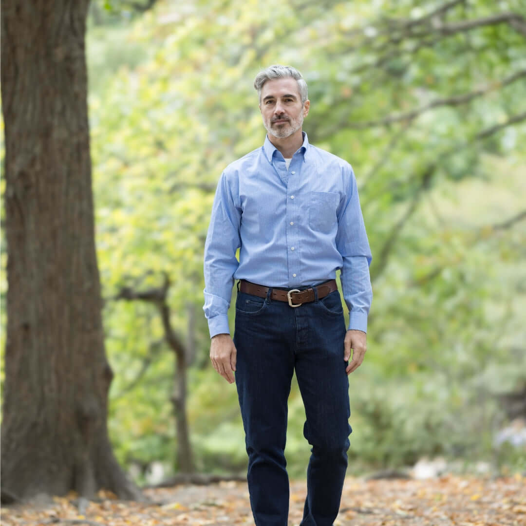 Man wearing a blue long sleeve button down collar shirt with magnetic closures, standing outdoors among trees.