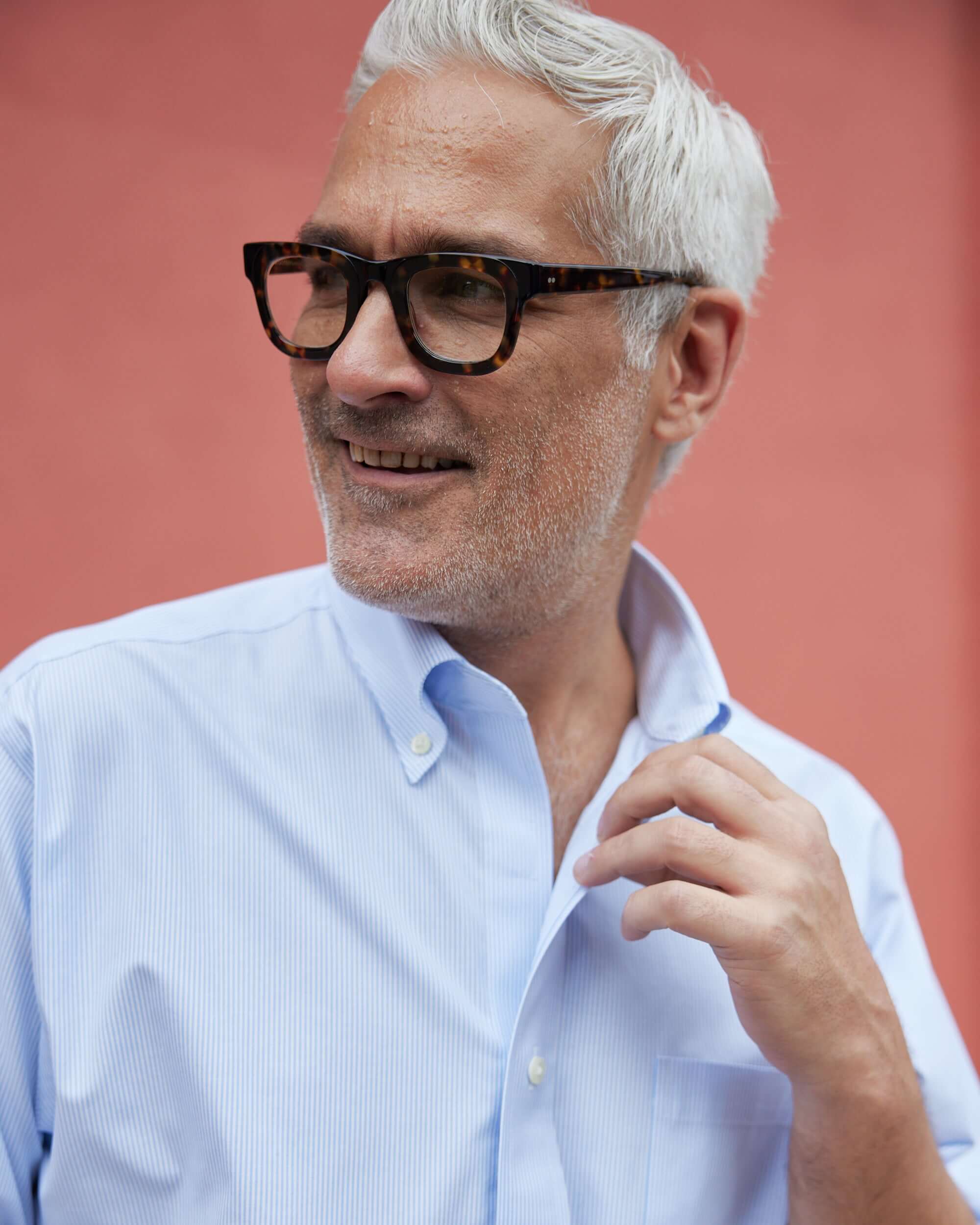 Man smiling in a light blue and white stripe Brooks Brothers polo with button-down collar.