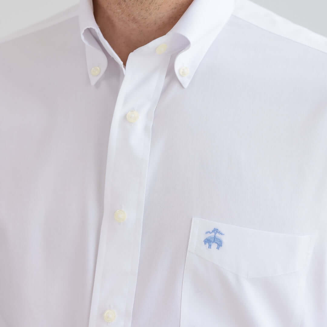 Close-up of a white button-down polo featuring a chest pocket with an embroidered logo.
