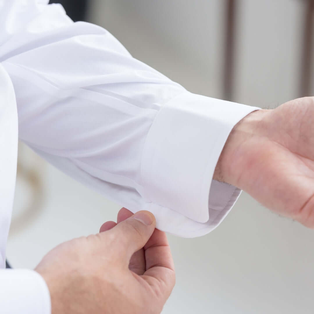 Close-up of a hand adjusting the cuff of a white Brooks Brothers X MagnaReady polo shirt.