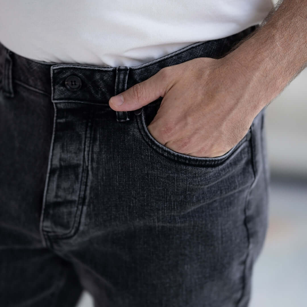 Close-up of a man wearing black wash five pocket jeans with hand in pocket, showcasing comfort and adaptive design.