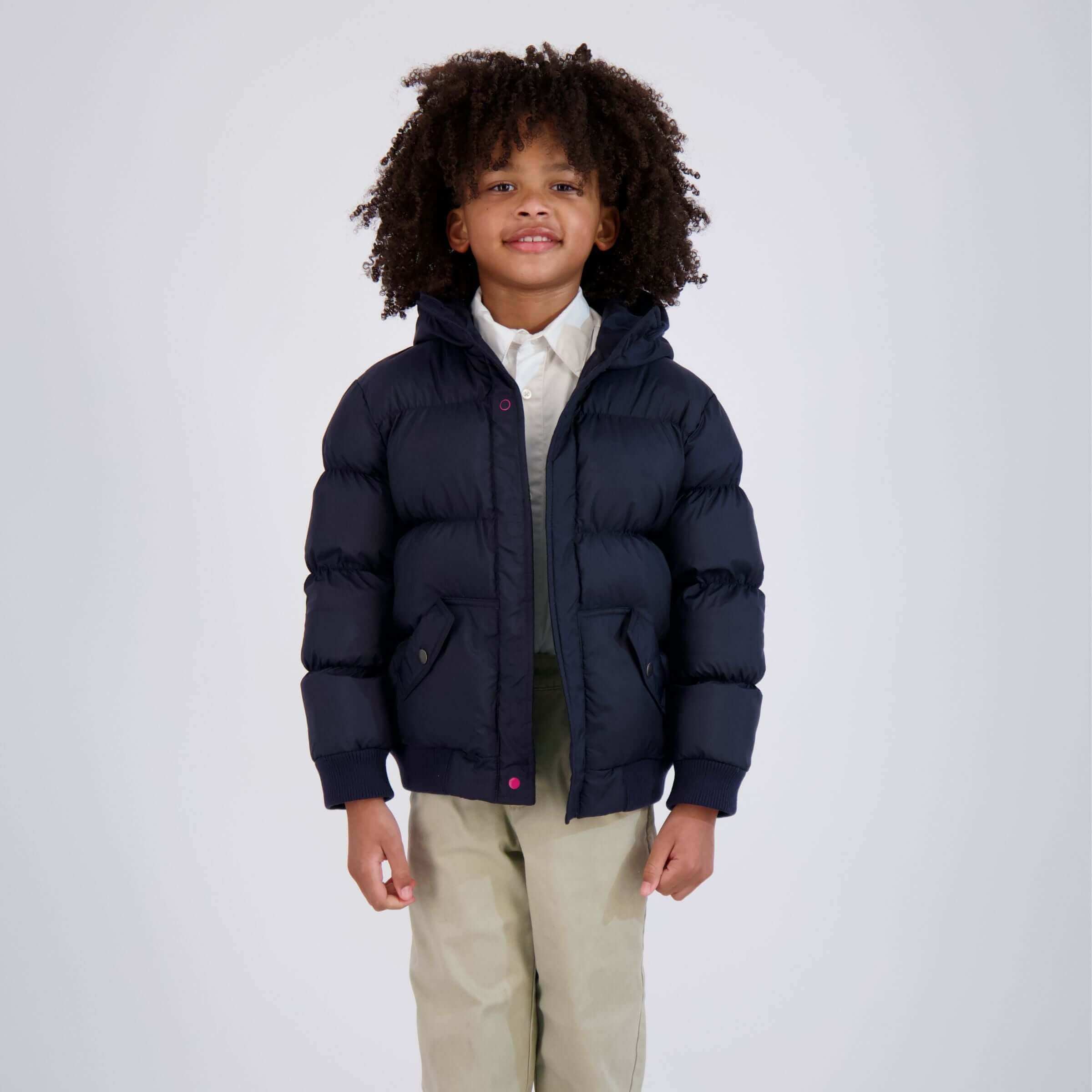 Smiling child in navy puffer coat with hood, showcasing easy magnetic closure design for independent dressing.
