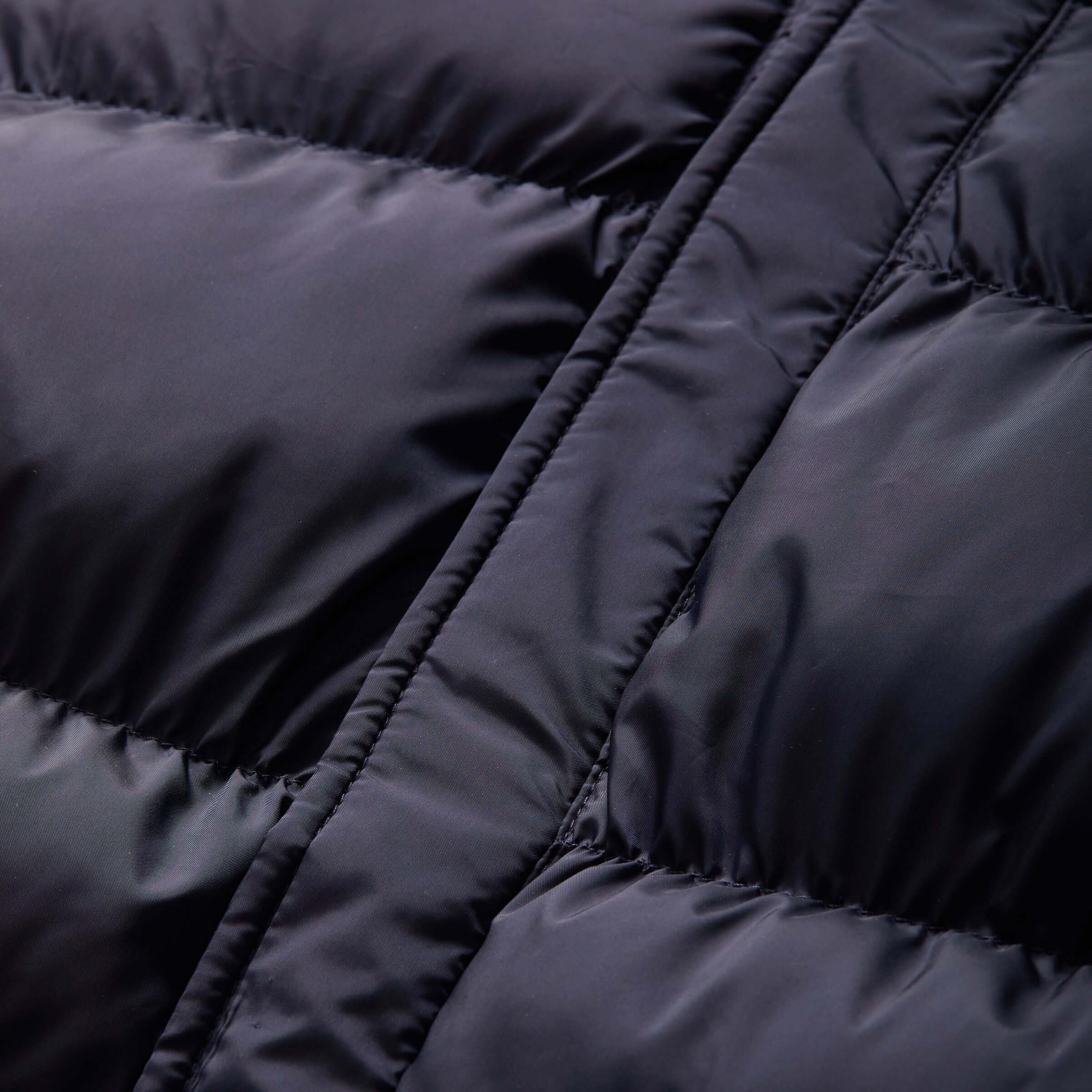 Close-up of navy water-resistant puffer coat fabric, showcasing its cozy quilted design and texture.