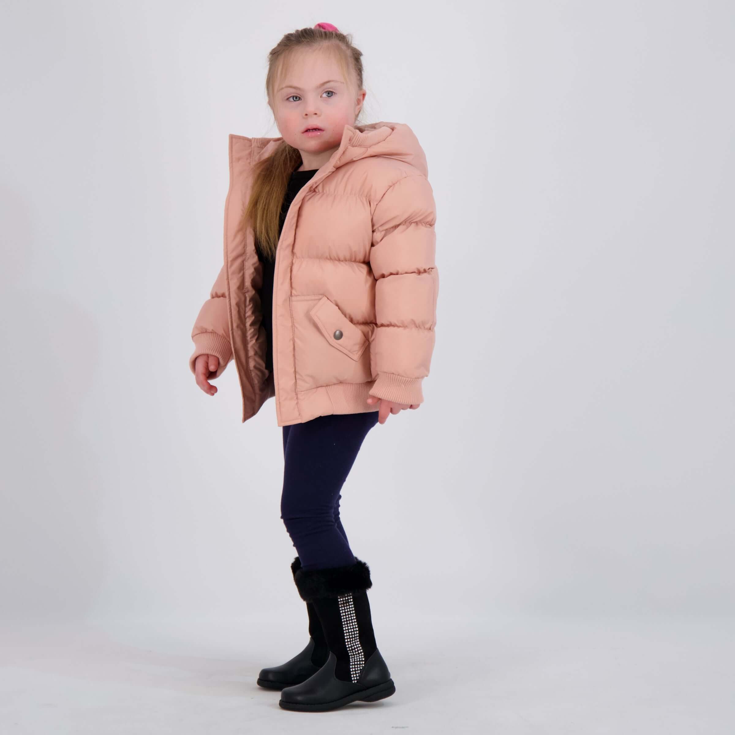 Young girl wearing a pink water-resistant puffer coat with hood, showcasing easy magnetic closure for independent dressing.