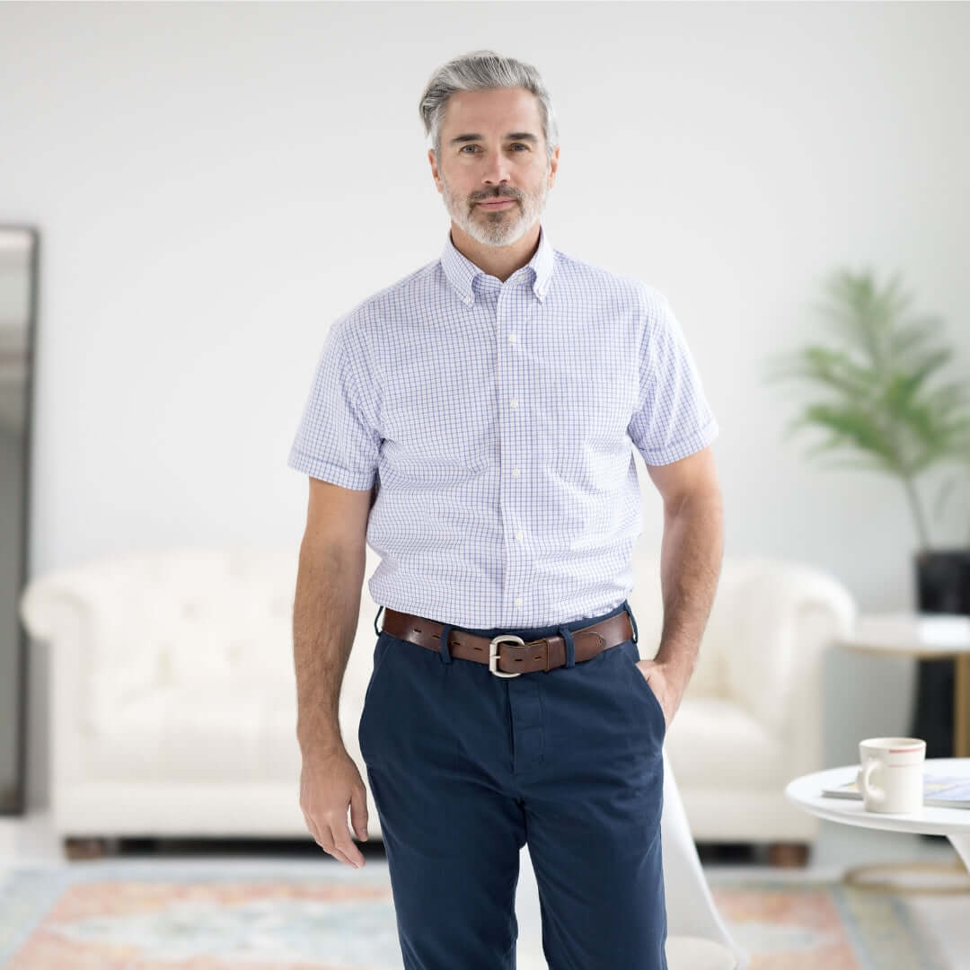 Man wearing a short sleeve red, white and blue button-down shirt styled with navy pants in a modern living space.