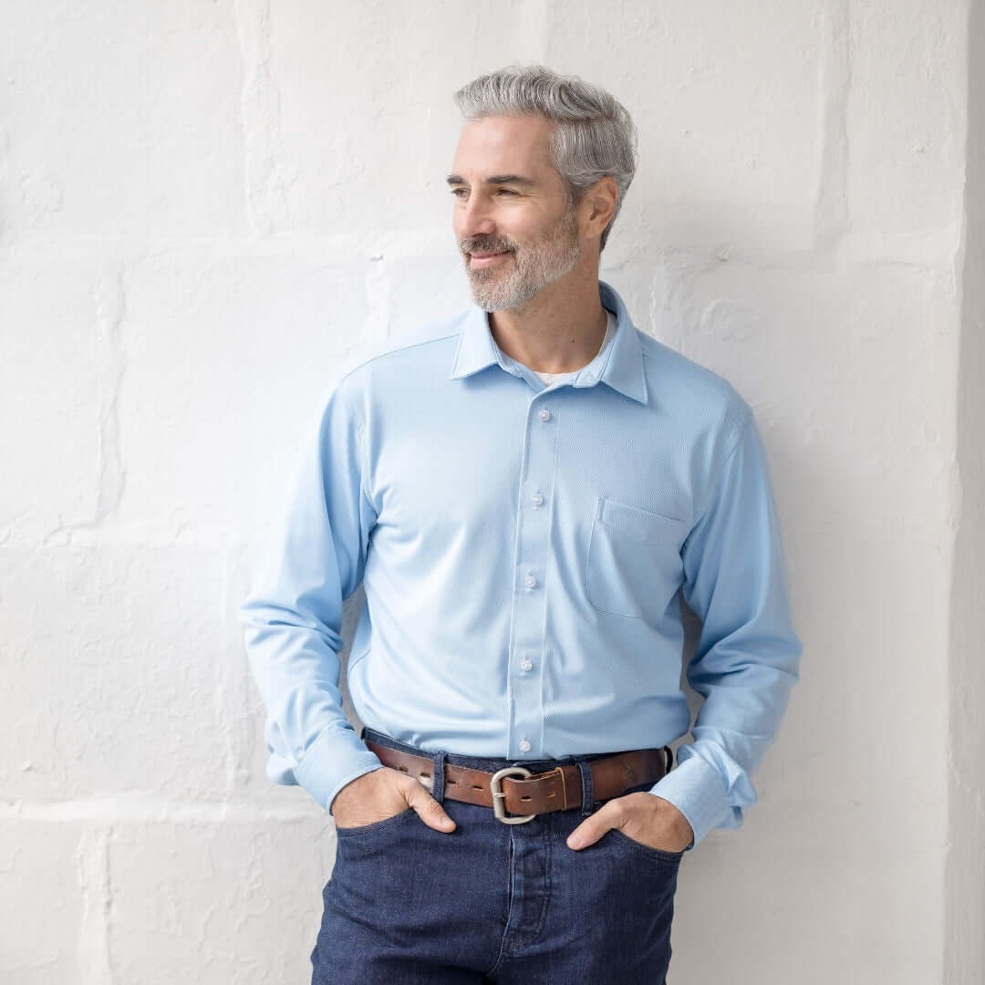 Man in a light blue long sleeve magnetic front shirt with pocket, against a textured wall.