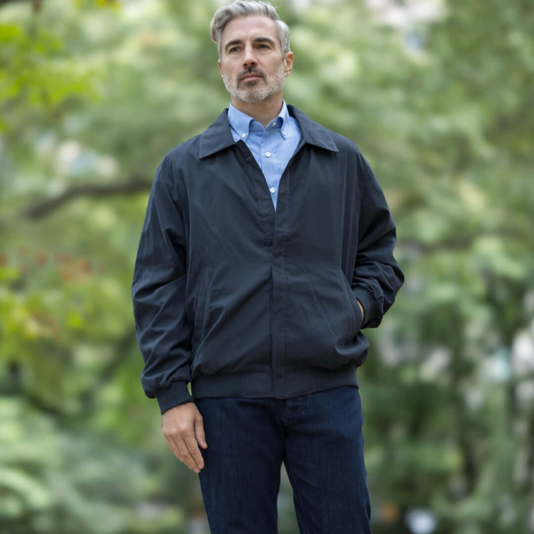 Man wearing a navy weatherproof golf jacket in an outdoor park setting.
