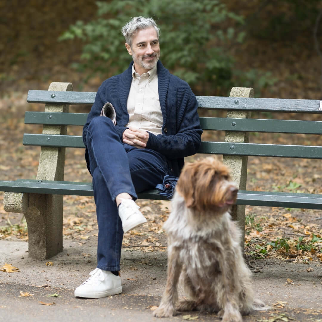 Man wearing navy ribbed cardigan relaxing on a park bench with a dog.