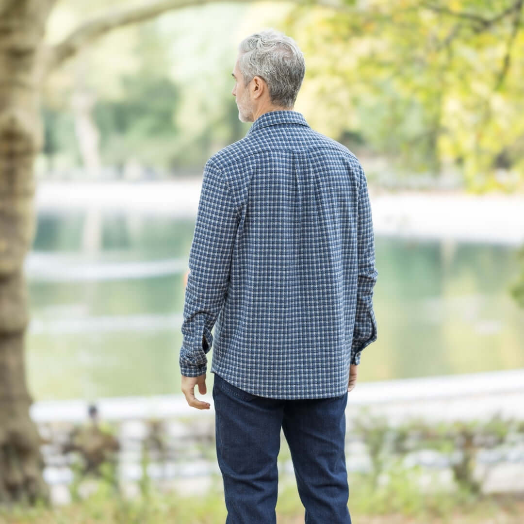 Man wearing an adaptive long sleeve white and navy check flannel shirt outdoors by a serene lake.