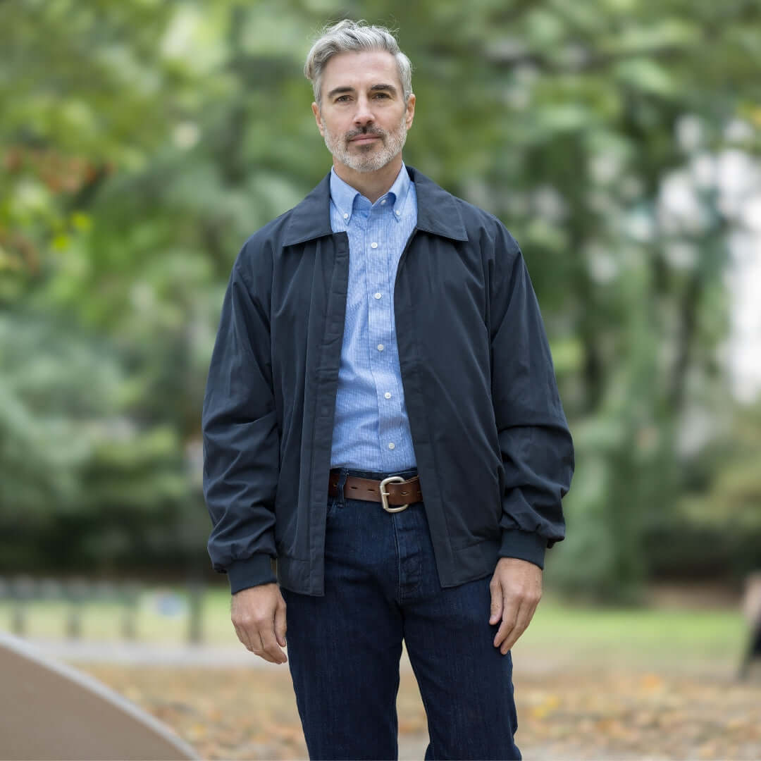 Man wearing blue long sleeve button-down shirt under black jacket in outdoor setting.