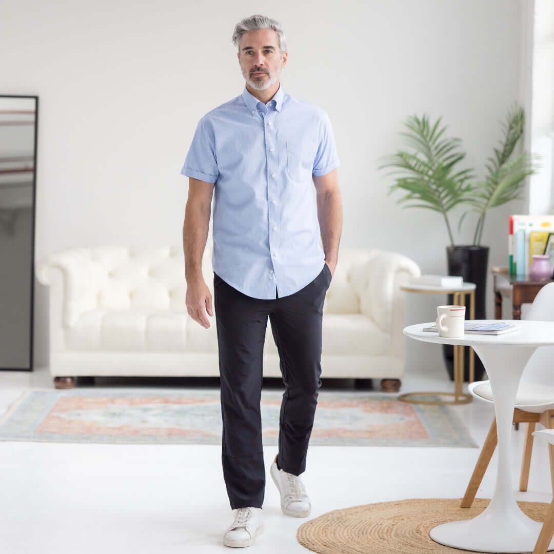 Man in light blue short-sleeve button-up shirt and black adaptive track pants, walking in a stylish interior.