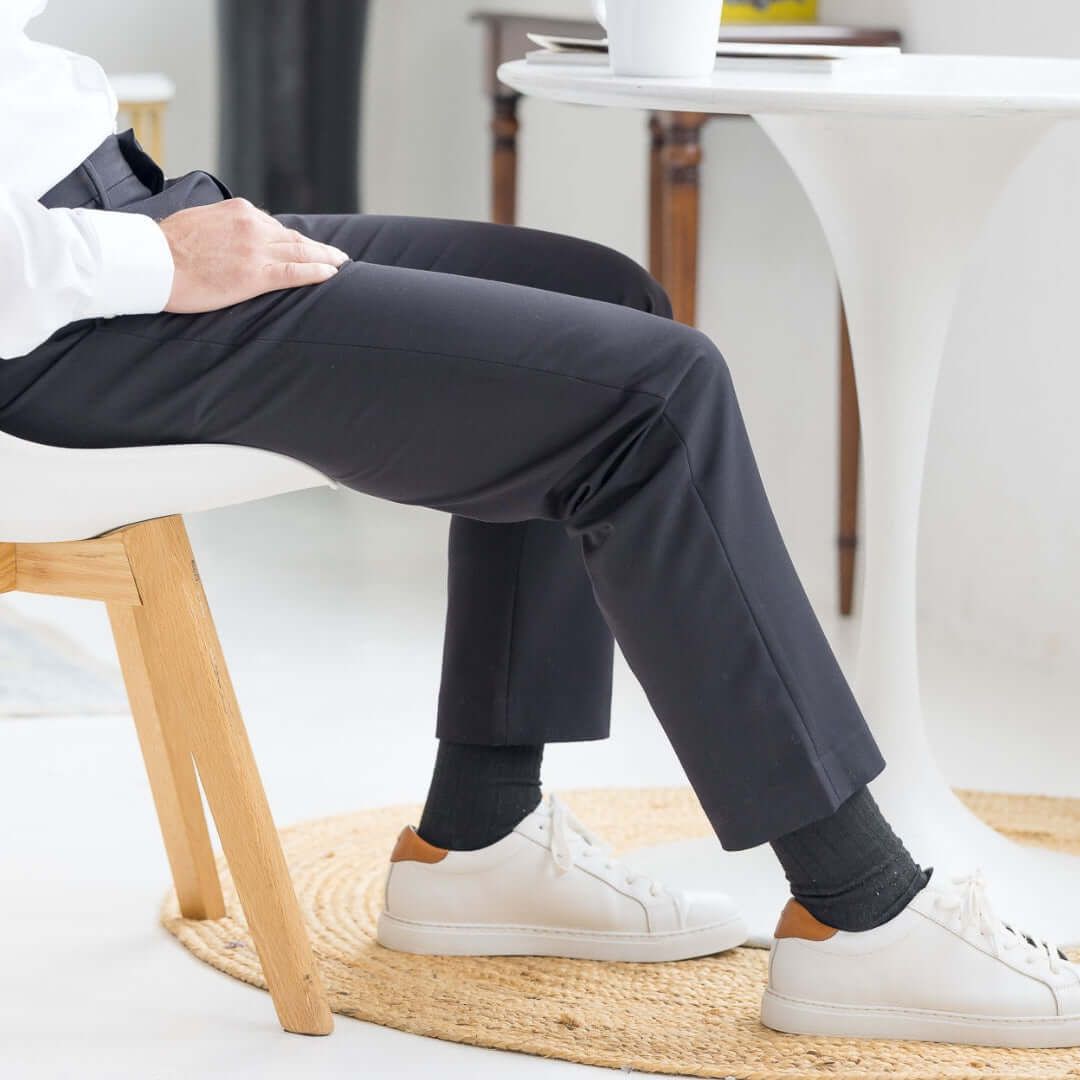 Men's adaptive black dress pant by Nautica x MagnaReady, paired with white sneakers and seated on a chair.