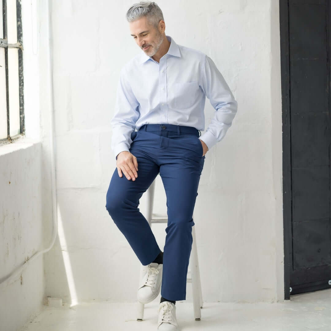 Man sitting on a stool wearing Nautica x MagnaReady Adaptive Navy Dress Pants and a light blue shirt.