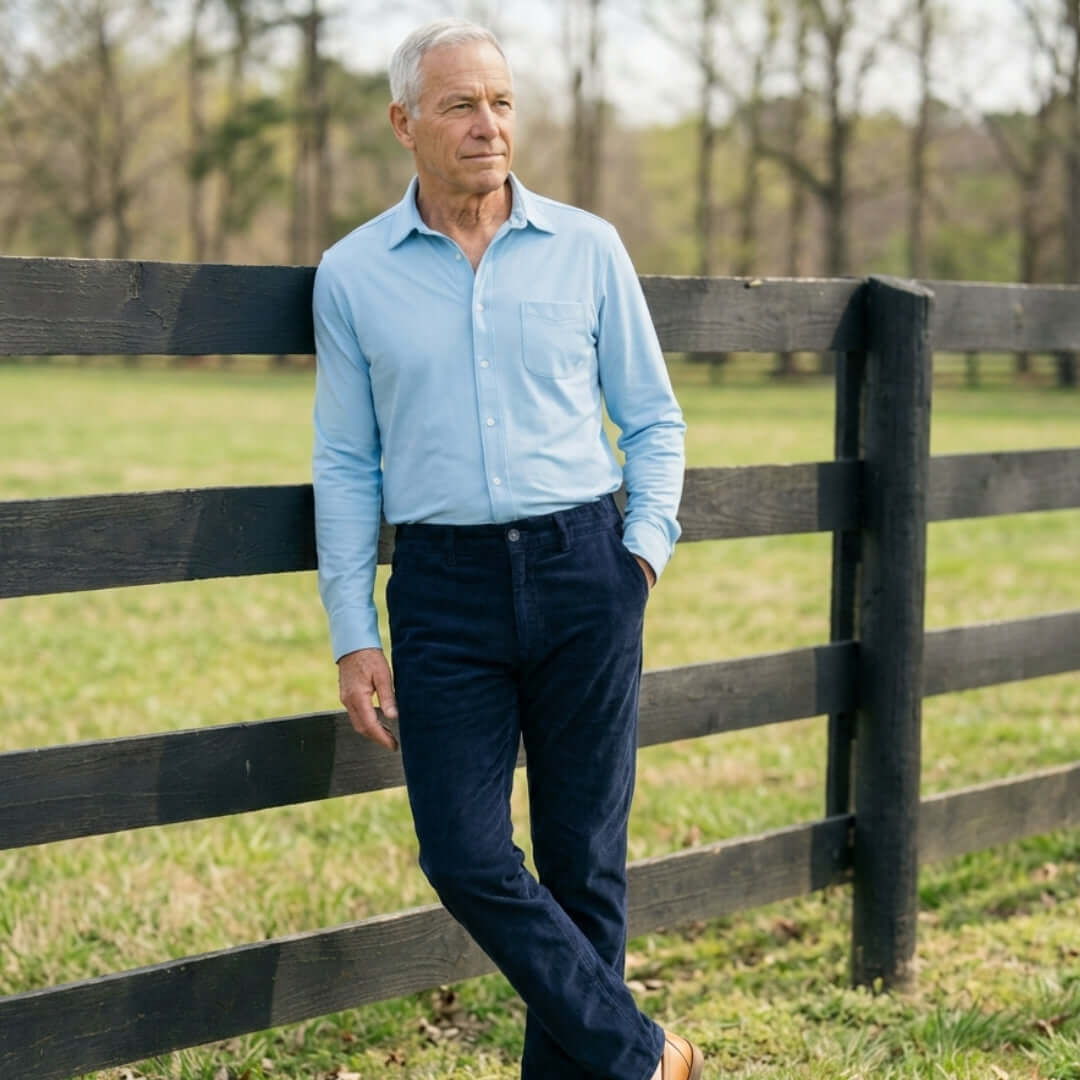 Man in a blue shirt and Navy Fine Wale Adaptive Corduroy Magnetic Fly Front Pant leaning against a fence.
