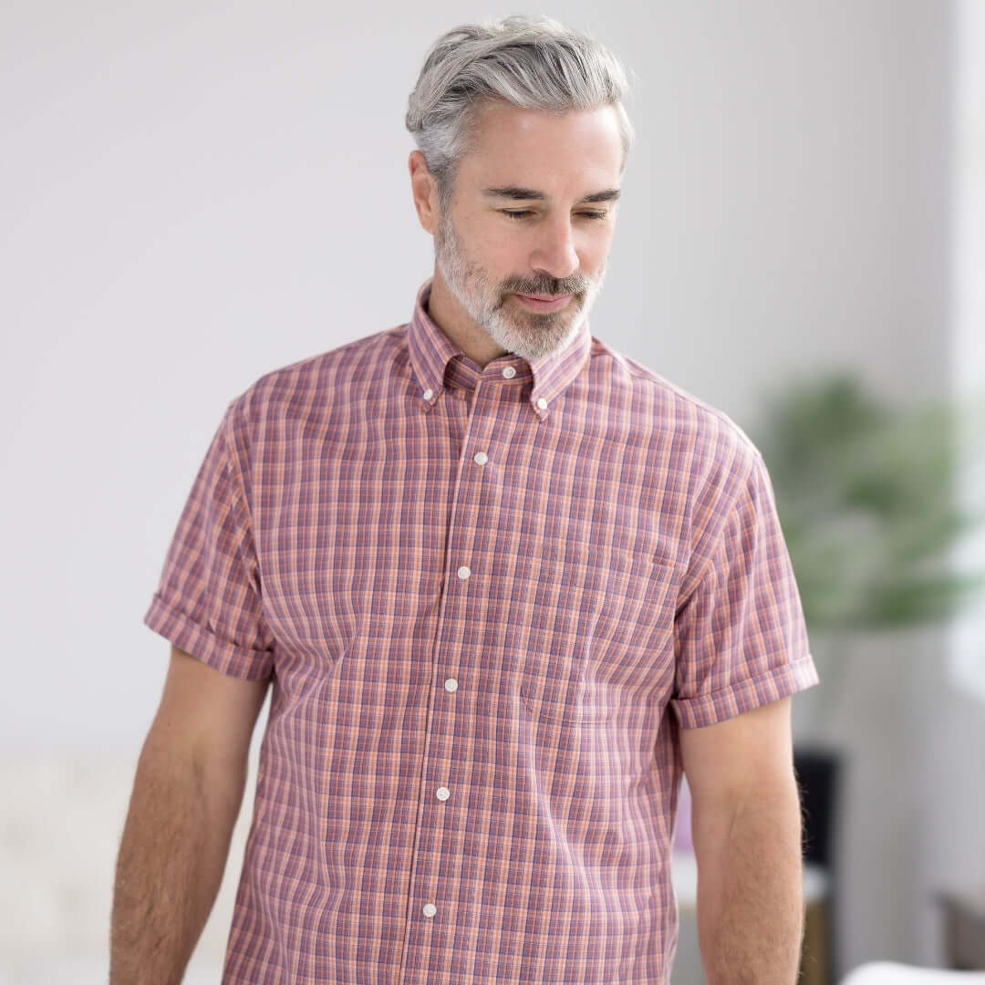 Man wearing an orange plaid short sleeve button-down collar shirt with magnetic closures, featuring a traditional fit.