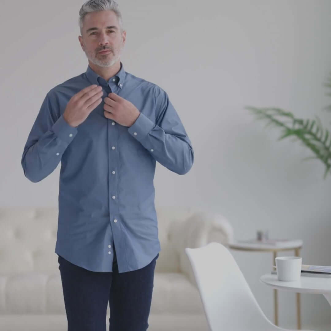 Man adjusting a blue chambray shirt with magnetic closures, showcasing adaptive fashion for easy dressing.