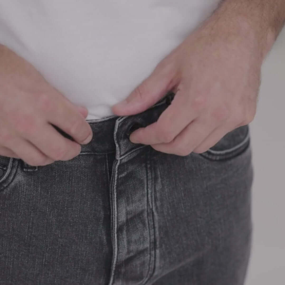 Person adjusting the magnetic fly on black wash five pocket adaptive jeans for easier dressing.