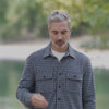 Man wearing a stylish adaptive long sleeve white and navy check flannel shirt by a serene lake setting.