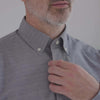 Model adjusting collar of a navy plaid button-down shirt with adaptive magnetic closures, perfect for limited mobility.