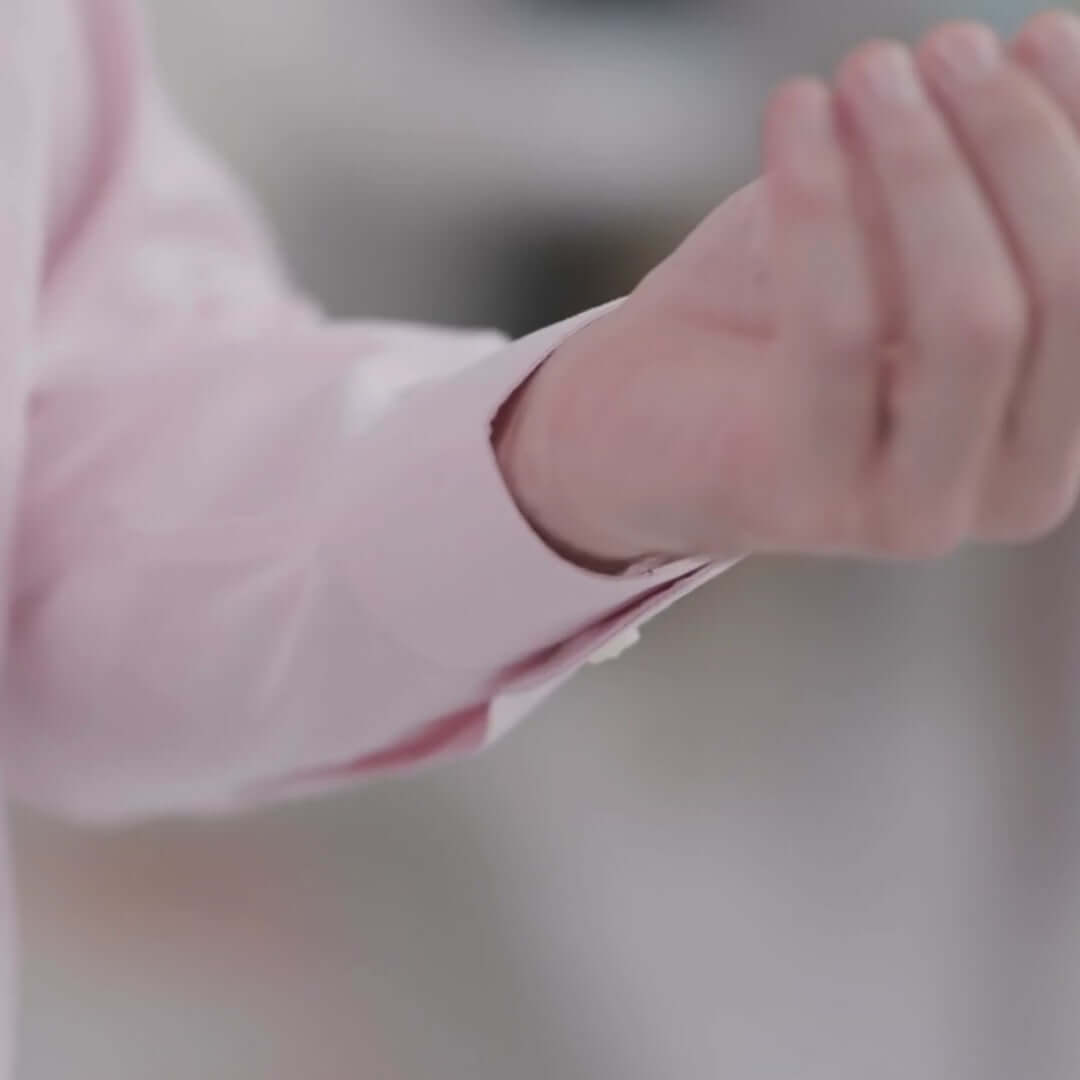 Close-up of a hand adjusting the cuff of a pink Brooks Brothers long sleeve polo shirt.