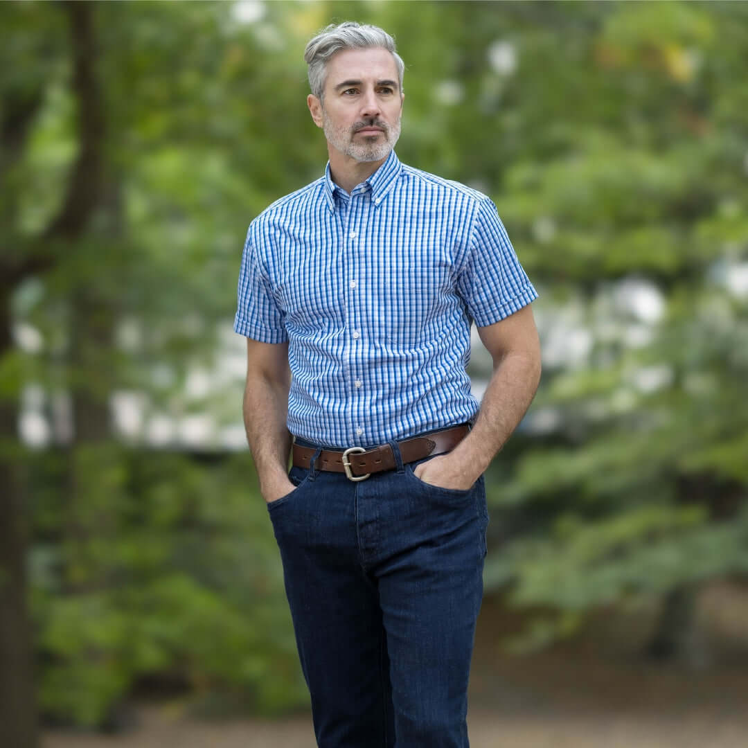Man wearing a short sleeve blue and white check cotton shirt in a park setting.
