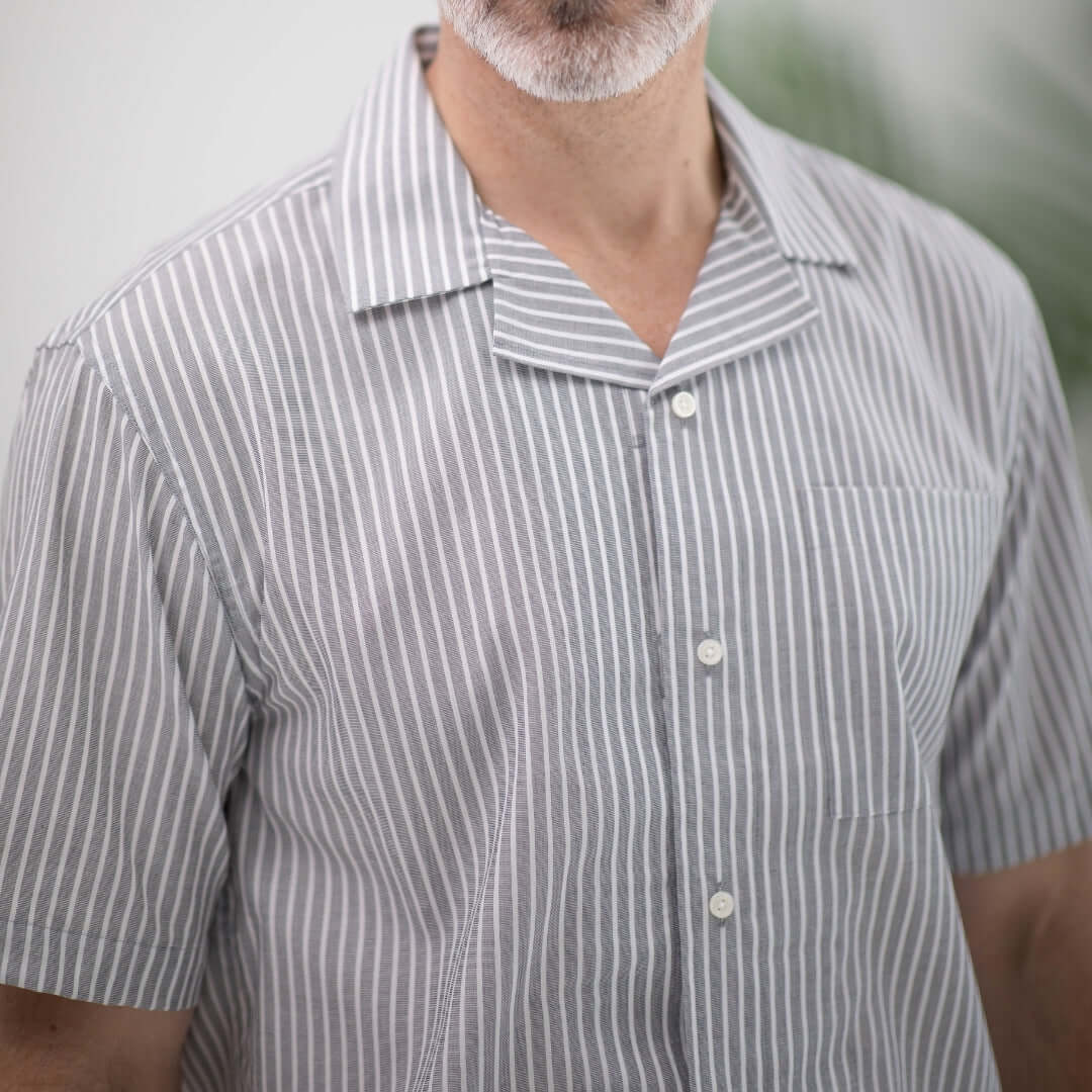 Close-up of a man wearing a short sleeve grey striped camp collar shirt with a pocket.