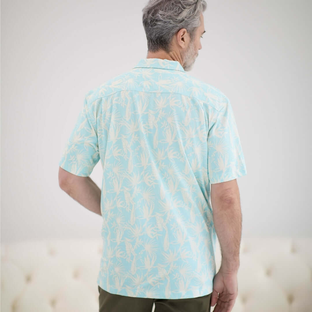 Back view of a man wearing a blue leaf patterned untucked short sleeve cooling shirt, designed for comfort and mobility.