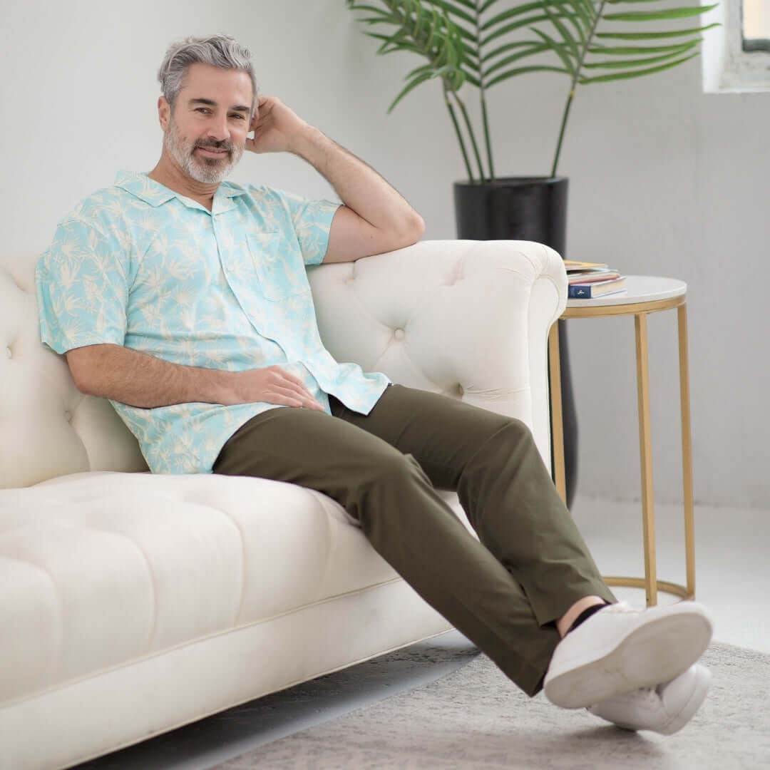Man sitting on a sofa wearing a blue leaf printed short sleeve cooling shirt, showcasing casual comfort and style.