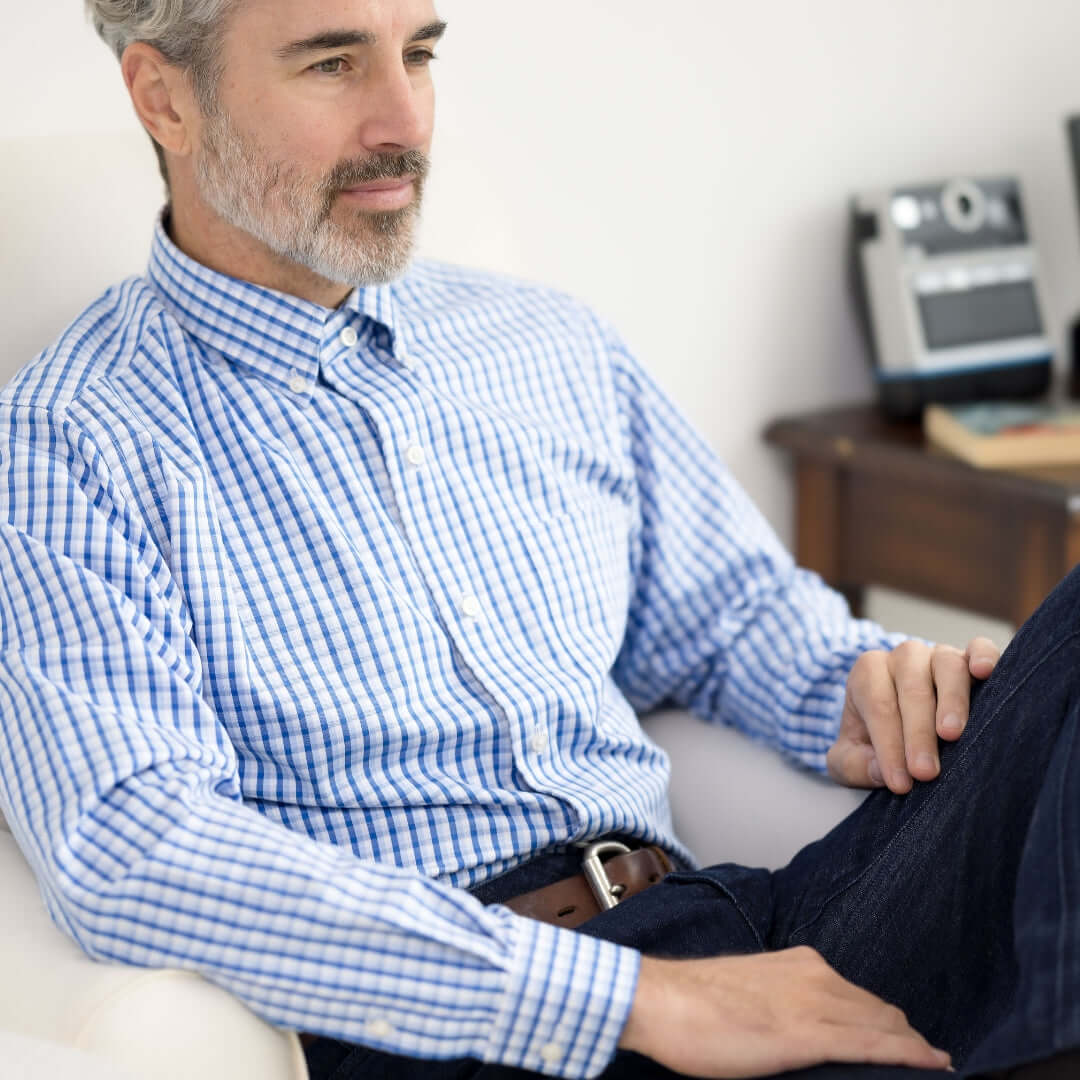 Man wearing a white and blue plaid long sleeve button-down collar shirt with magnetic closures, seated comfortably.