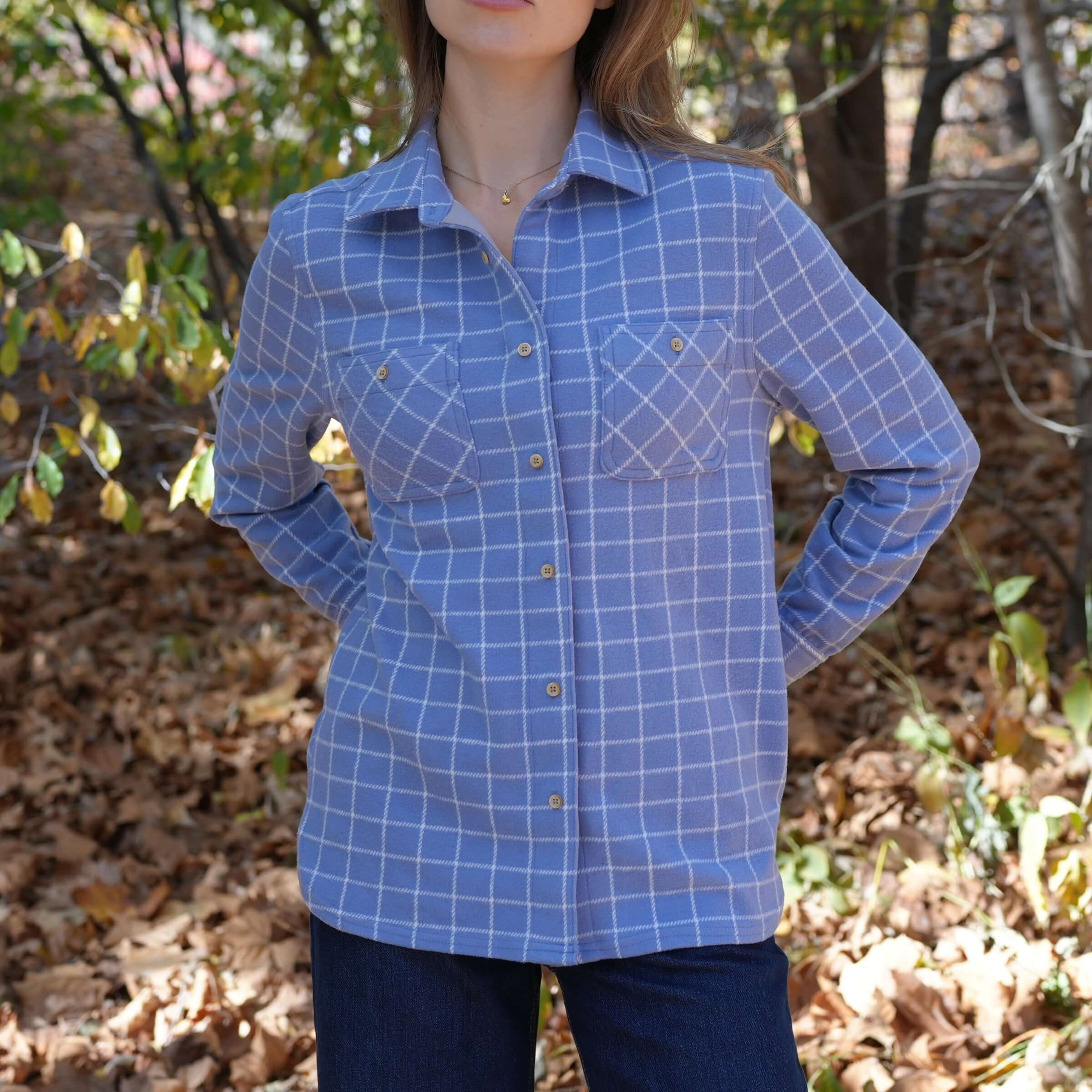 Woman wearing a blue and white checkered flannel shirt with button pockets in a forest setting.